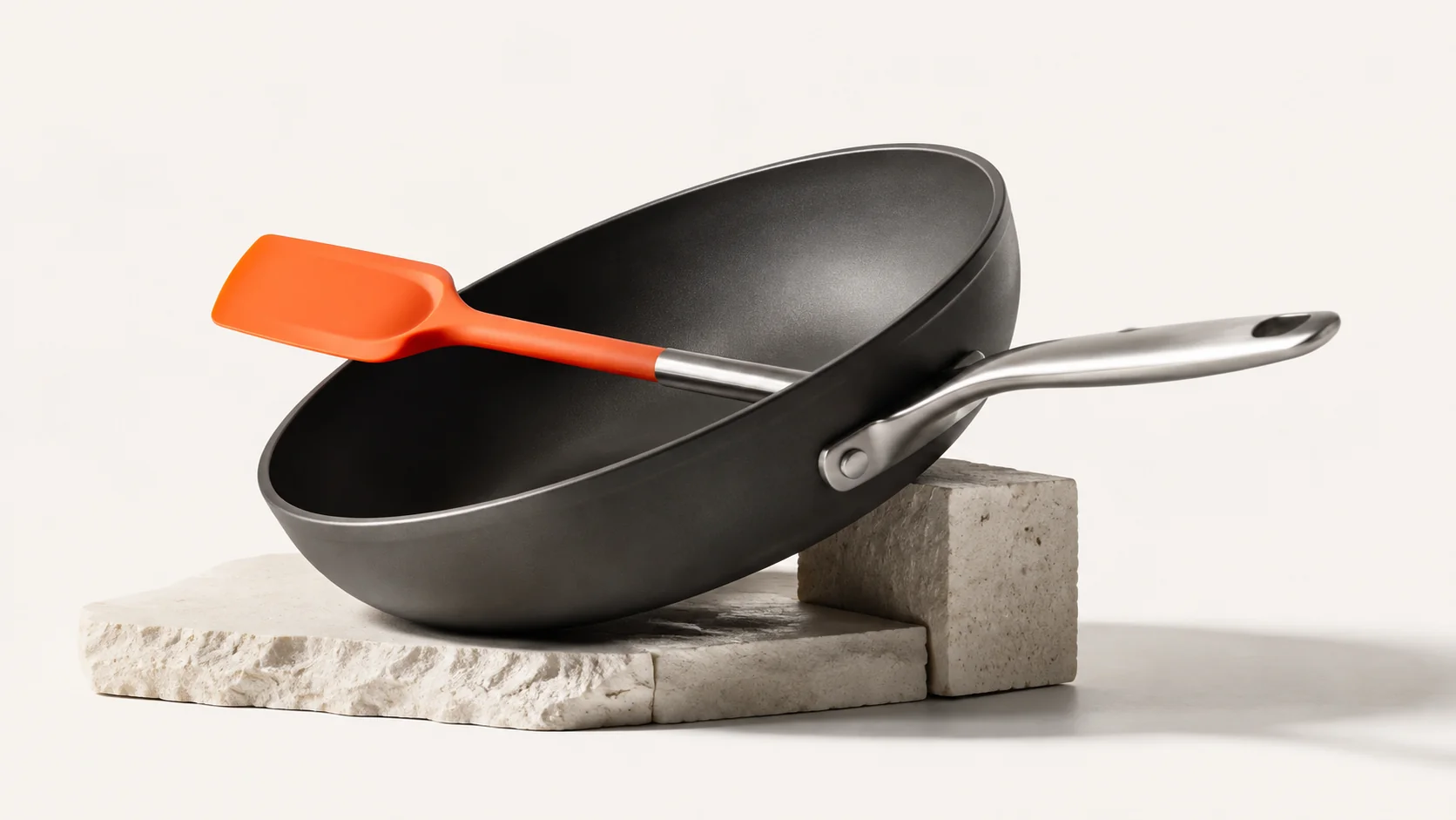Editorial illustration: a charcoal chef's pan with an orange spatula on a stone block